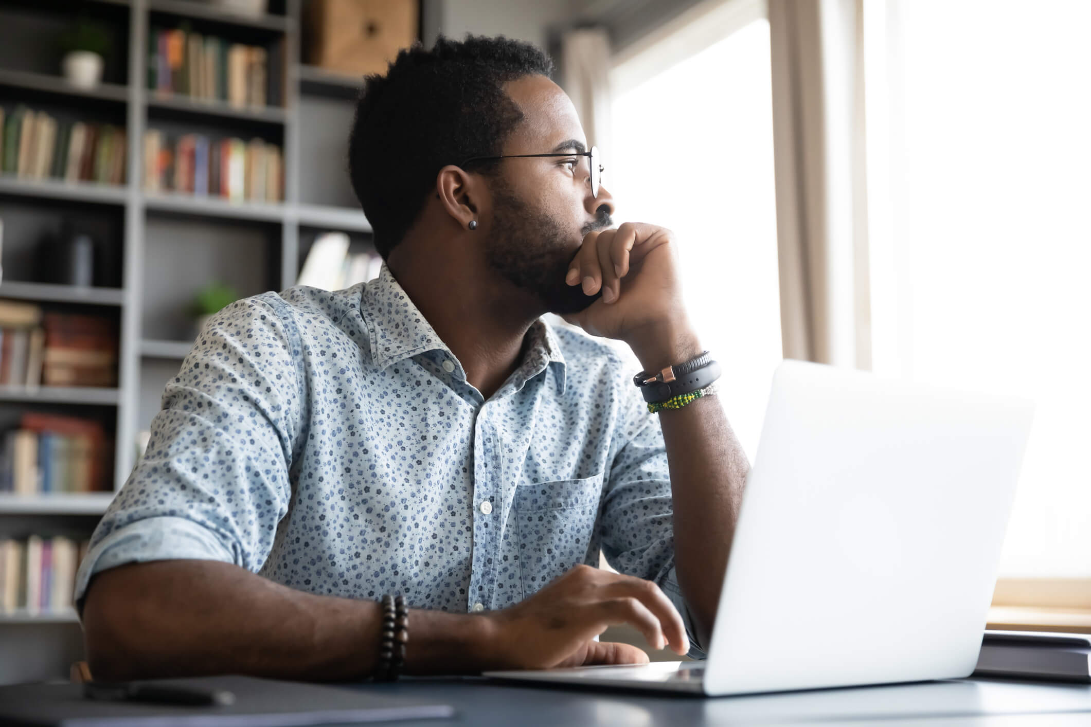 Thoughtful serious african professional business man sit with laptop thinking of difficult project challenge looking for problem solution searching creative ideas lost in thoughts at home office desk