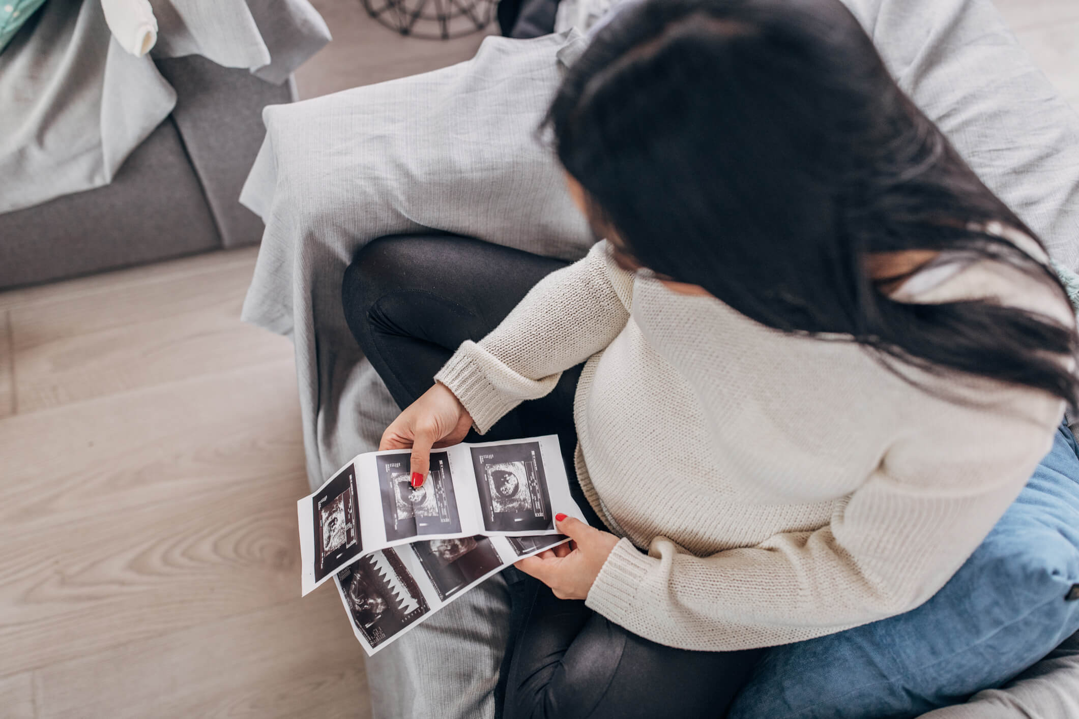One woman, beautiful pregnant woman sitting at home, holding ultrasound pictures.