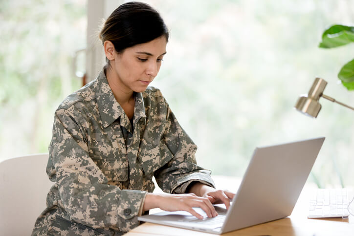 A mid adult female soldier wearing her uniform works on her laptop at home.