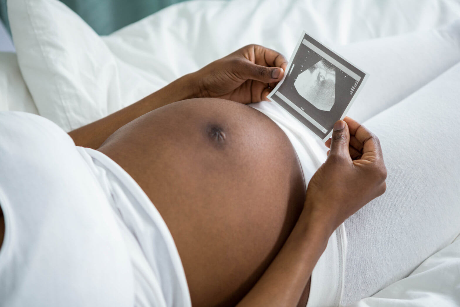 Pregnant woman looking at ultrasound pictures lying on her bed