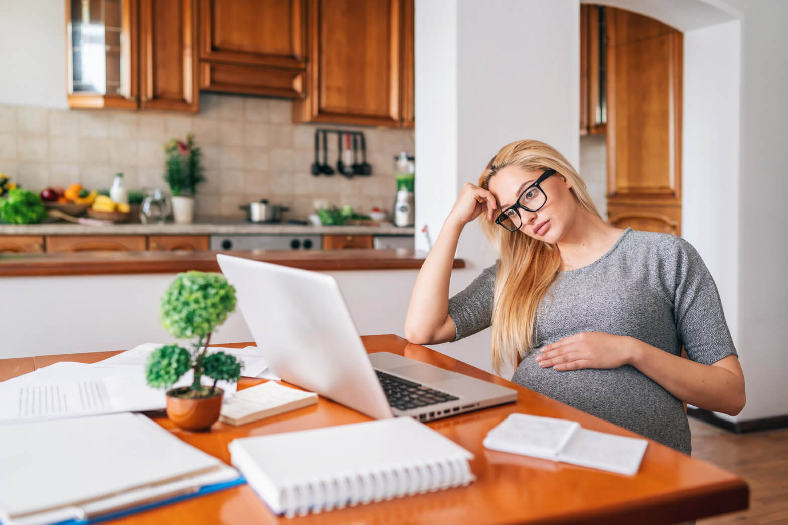 Blond pregnant woman working at home, using laptop.